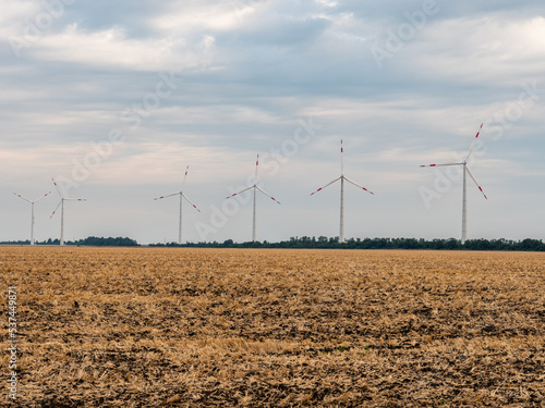 A row of windmills (wind turbines with rotating blades) against the backdrop of autumn field. Adyghe wind farm from many towers of wind turbines. Wind power complex of Rosatom. photo