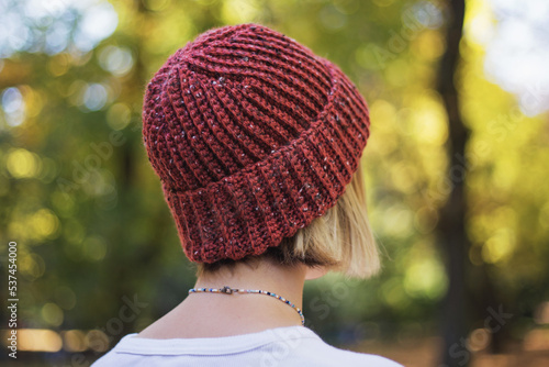 Woolen crocheted red beanie, slow fashion concept. Unisex woolen knitted hat. Woman in a red hat walking in the park

