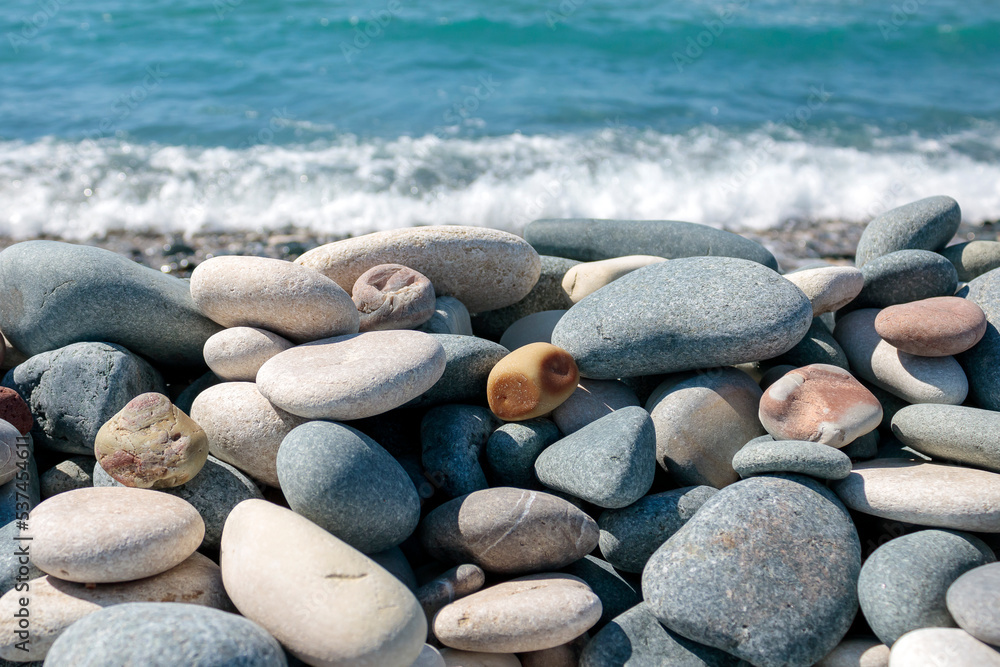 Close-up of beach stones and pebbles in front of blurred blue sea wave Close-up of beach stones and pebbles in front of blurred blue sea wave