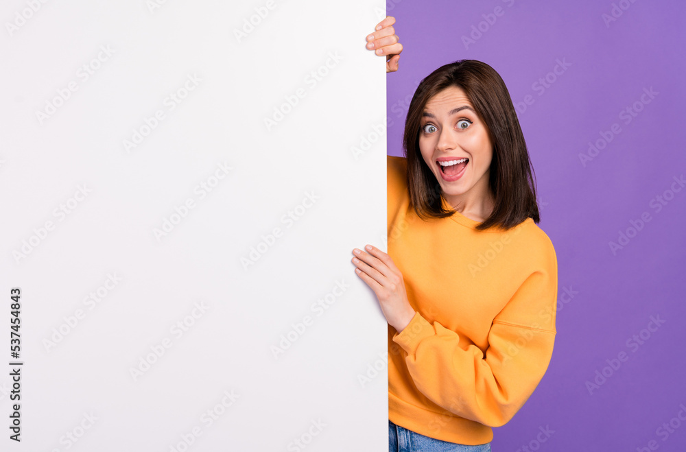 Photo of overjoyed positive lady wear orange trendy pullover hiding big card banner empty space isolated purple color background Photo of overjoyed positive lady wear orange trendy pullover hiding big card banner empty space isolated purple color background