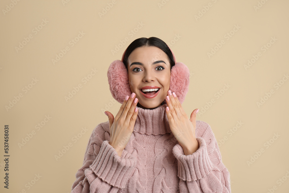 Beautiful young woman wearing earmuffs on beige background Beautiful young woman wearing earmuffs on beige background