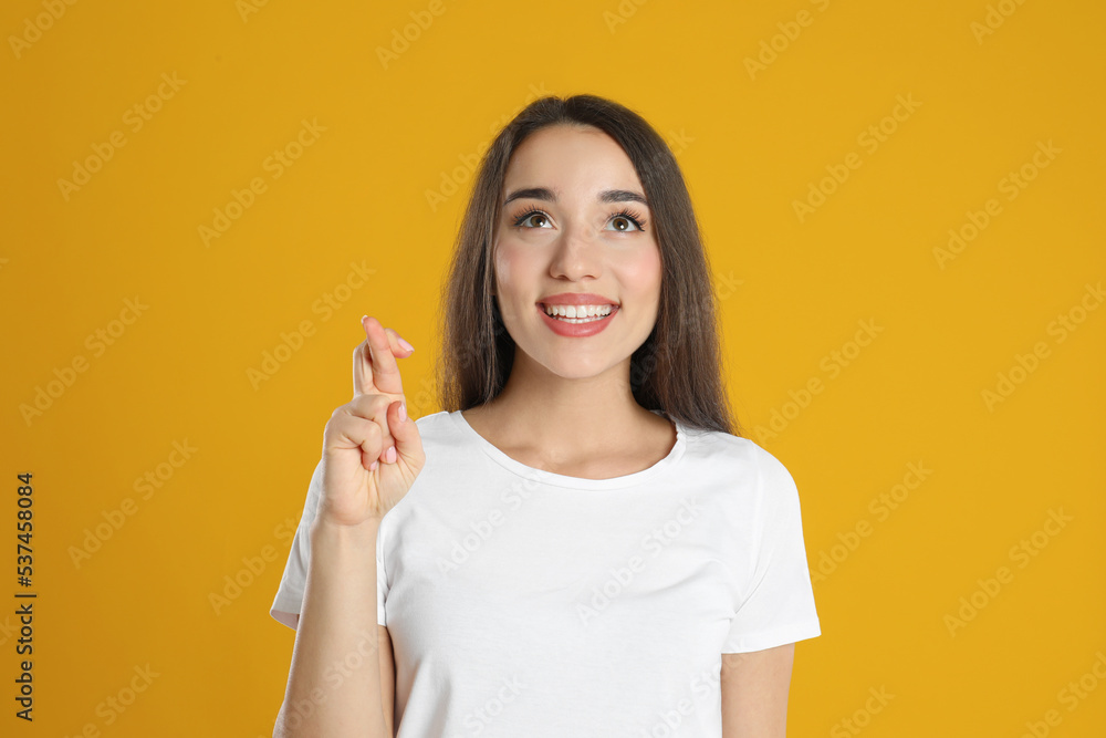 Excited young woman holding fingers crossed on yellow background. Superstition for good luck Excited young woman holding fingers crossed on yellow background. Superstition for good luck