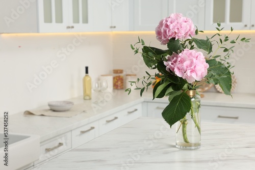 Beautiful pink hortensia flowers in vase on kitchen table. Space for text