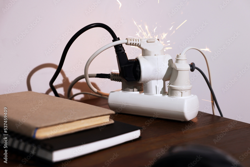 Inflamed plug in power strip indoors on wooden table. Electrical short circuit Inflamed plug in power strip indoors on wooden table. Electrical short circuit
