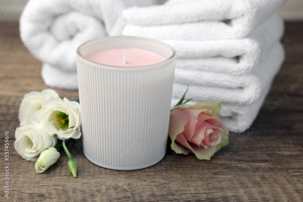 Scented candle, folded towels and flowers on wooden table Scented candle, folded towels and flowers on wooden table