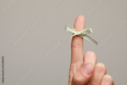 Woman showing index finger with tied bow as reminder on grey background, closeup. Space for text