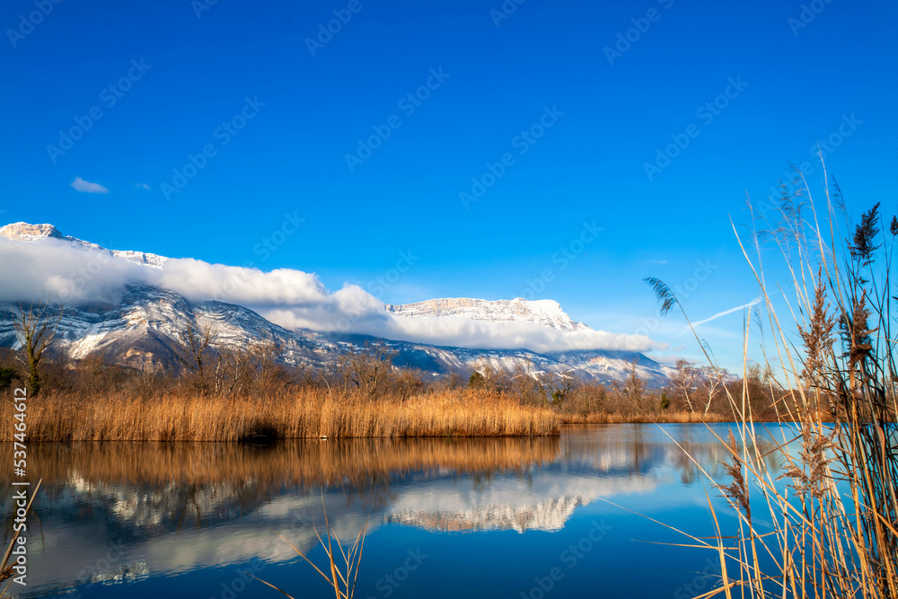 Fototapeta premium Varces et Allières France 11/2021 Etangs du Noiret, jeux de réflexion dans l'eau, reflets des montagnes enneigées, des roseaux et du ciel dans l'étang