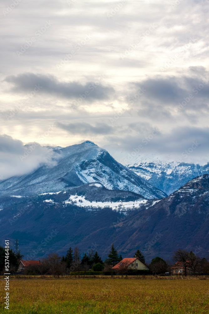 Fototapeta premium Varces et Allières France 11/2021 vue sur les montagnes enneigées, ciel orageux, nuageux, habitations au milieu des champs
