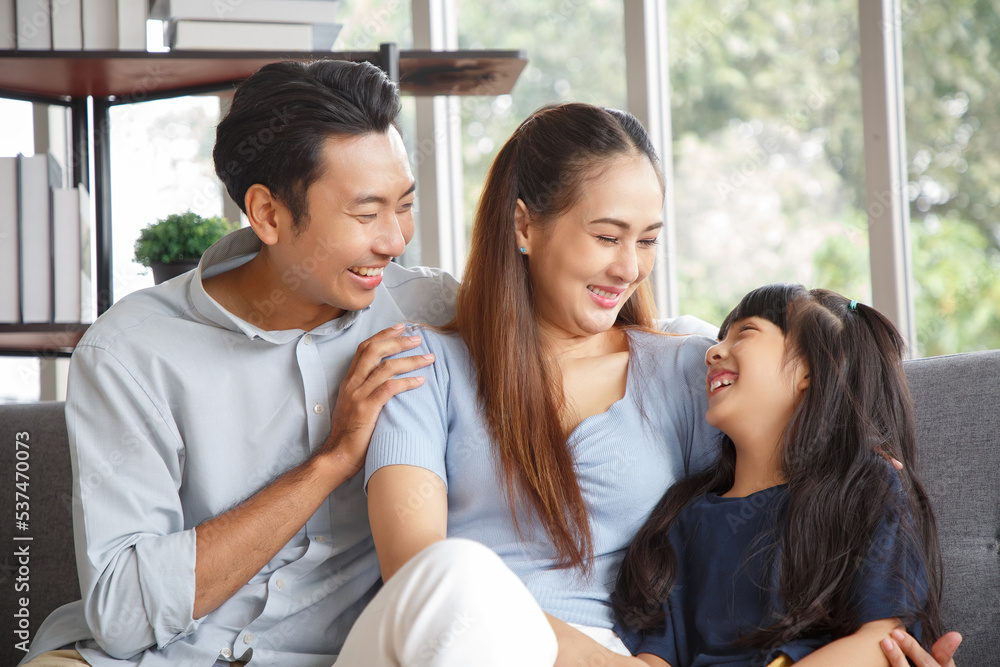 Portrait of a happy young family. Mom, dad and daughter look at the camera and smile. The faces of Asian parents and their child in living room. Portrait of a happy young family. Mom, dad and daughter look at the camera and smile. The faces of Asian parents and their child in living room.