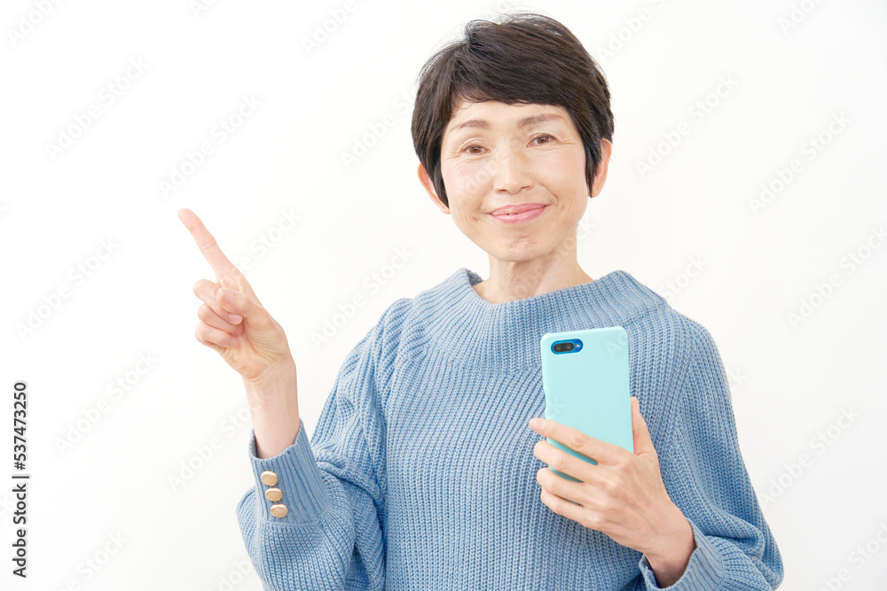 スマホを持って左を指差すシニア女性 白背景 スマホを持って左を指差すシニア女性 白背景