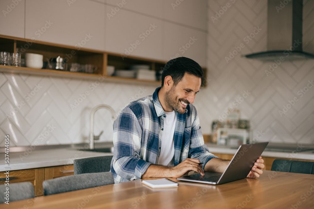 A male worker smiling and working online, over the laptop.