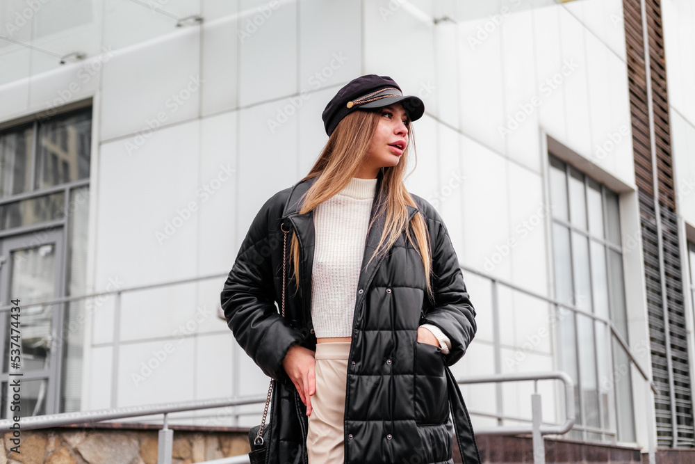 Elegant young woman in black coat and beret standing near office building looking away outdoor