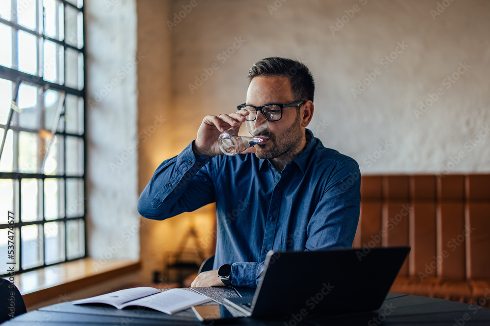 Businessman drinking a glass of water while working online, at the office. Businessman drinking a glass of water while working online, at the office.