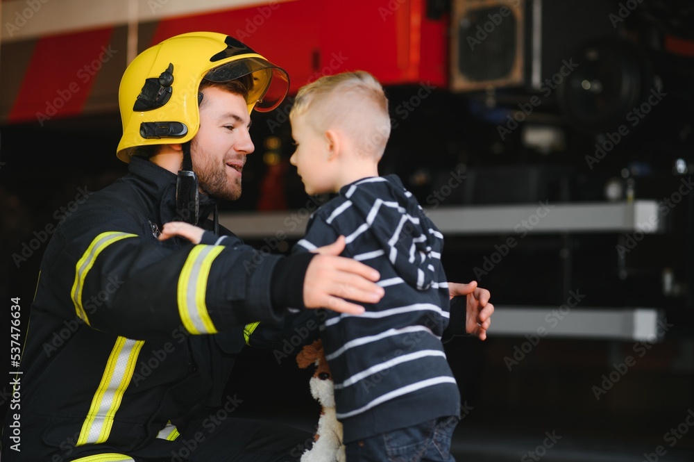 Portrait of rescued little boy with firefighter man standing near fire truck. Firefighter in fire fighting operation. Portrait of rescued little boy with firefighter man standing near fire truck. Firefighter in fire fighting operation.