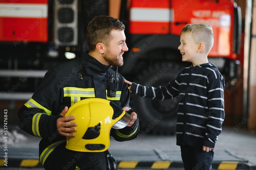 A firefighter take a little child boy to save him. Fire engine car on background. Fireman with kid in his arms. Protection concept. A firefighter take a little child boy to save him. Fire engine car on background. Fireman with kid in his arms. Protection concept.