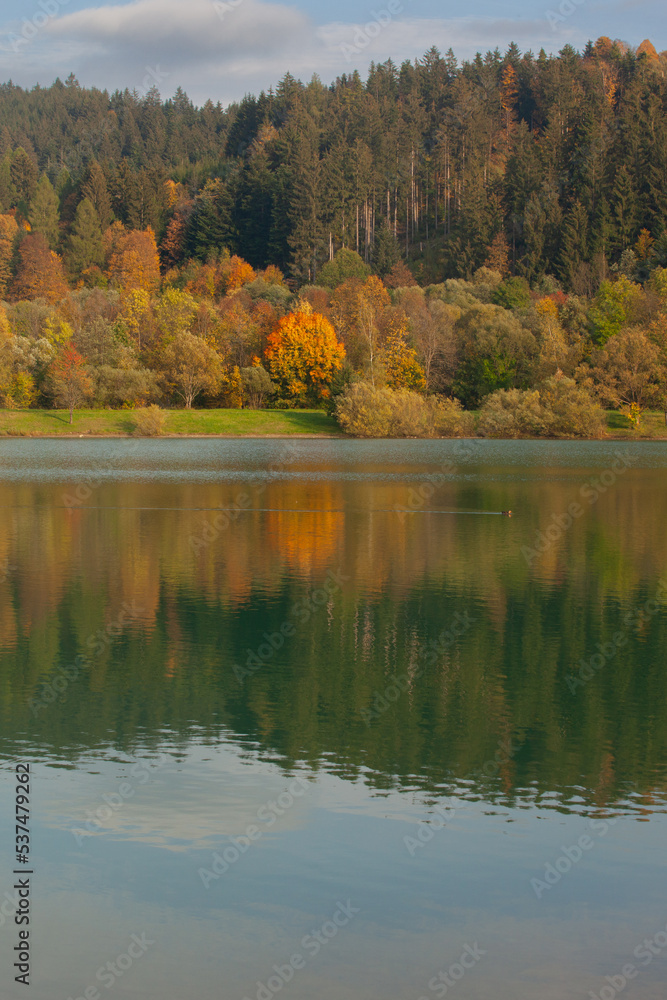 A mountain lake in autumn. The forest with autumn colors, yellow orange, is reflected in the lake as in a mirror. It is calm and tranquil.