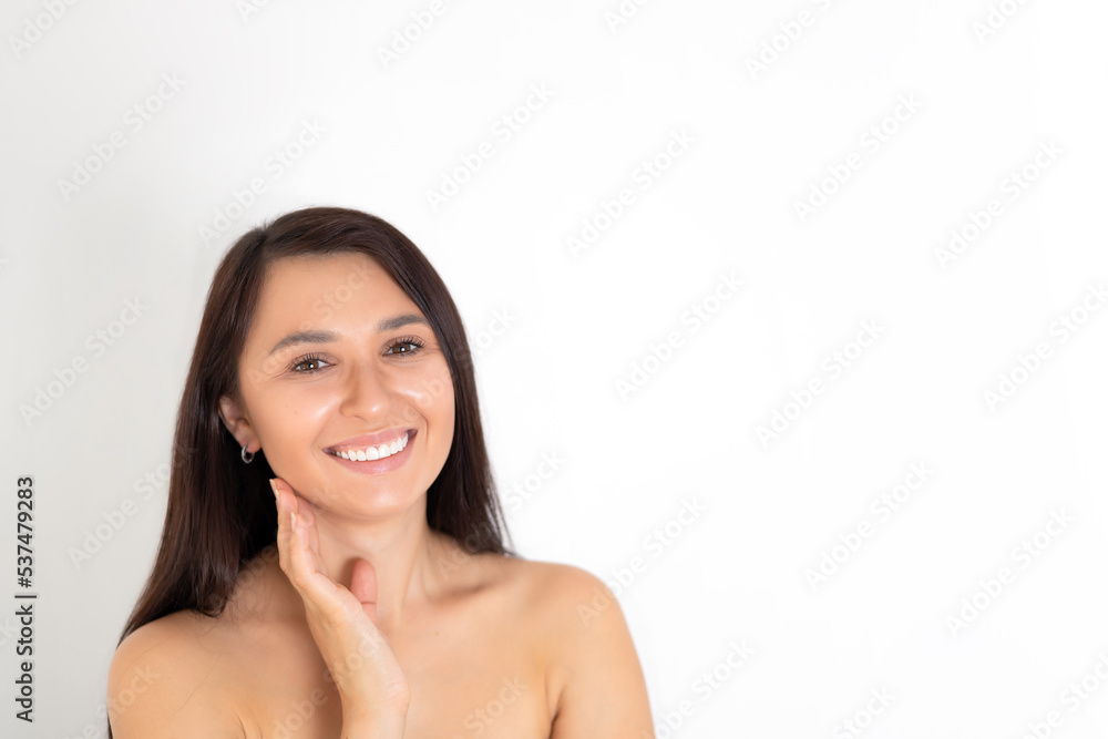 A natural portrait of a well-groomed young brunette woman with nude makeup. Gentle Beauty keeps her hands close to her face. White background place for text A natural portrait of a well-groomed young brunette woman with nude makeup. Gentle Beauty keeps her hands close to her face. White background place for text