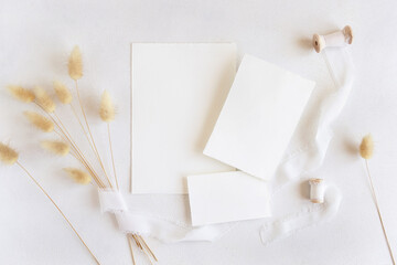 Blank cards near silk ribbons and dried hare's tail grass top view on white, boho mockup