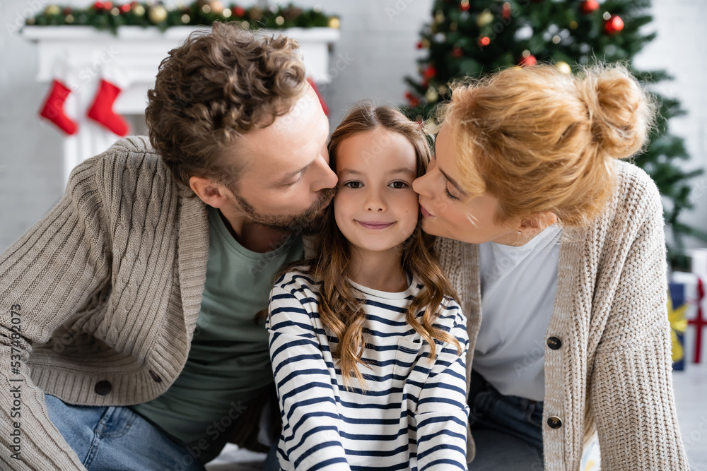 Parents kissing happy daughter during christmas at home Parents kissing happy daughter during christmas at home