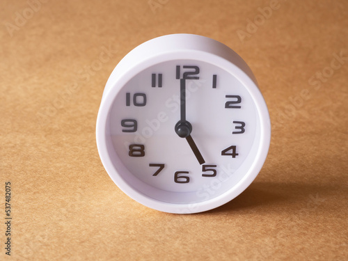 Close up, white clock shows time at 5 o'clock on the office brown workplace tabletop. Copy space for your text. Business and education concept..