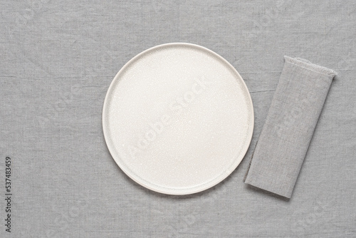Empty beige plate mockup with gray linen napkin on gray linen tablecloth. Top view, flat lay, copy space.