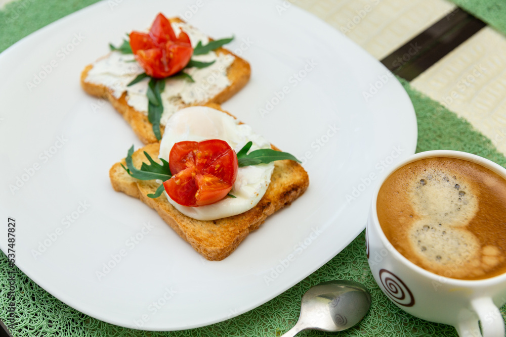 Breakfast with cup of coffee and whole wheat toasted bread with poached egg, tomato, arugula and cheese on white plate. Breakfast with cup of coffee and whole wheat toasted bread with poached egg, tomato, arugula and cheese on white plate.