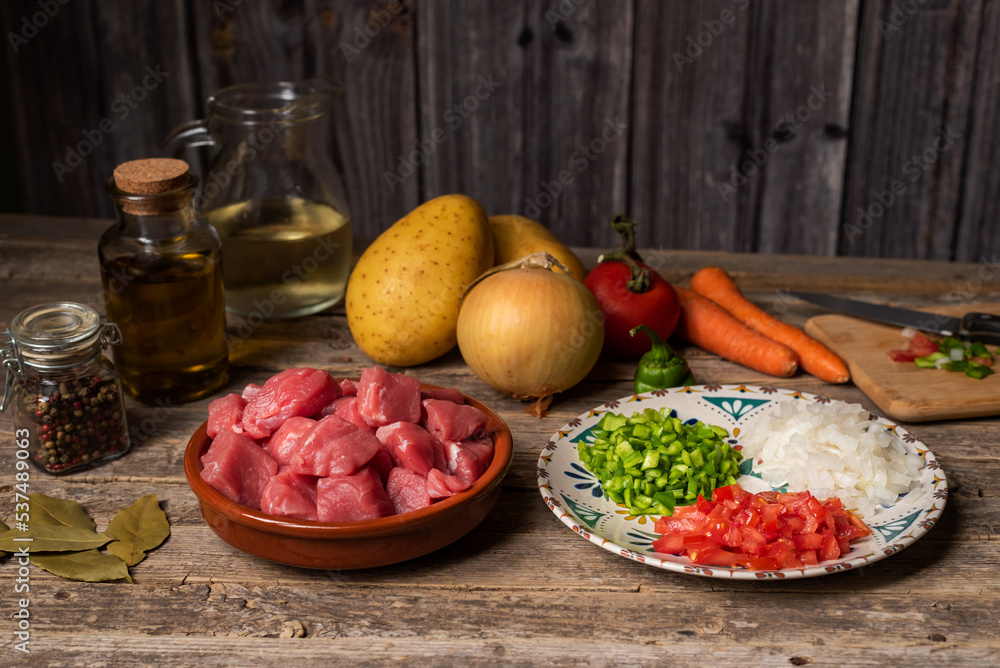 Ingredients for a beef stew,pieces of beef,potatoes,onions,peppers,carrots,tomatoes,oil,laurel and white wine,on an old wooden table.