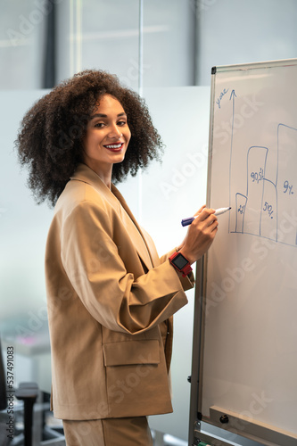 Curly-haired woman in beige suit writing something on the white board photo