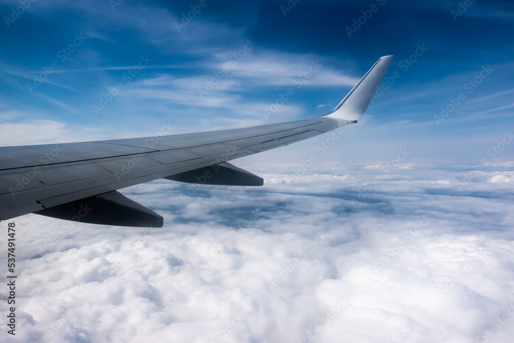 View from the plane window to the wing. Photo taken while flying above the clouds. In the distance, a visible horizon made of clouds View from the plane window to the wing. Photo taken while flying above the clouds. In the distance, a visible horizon made of clouds