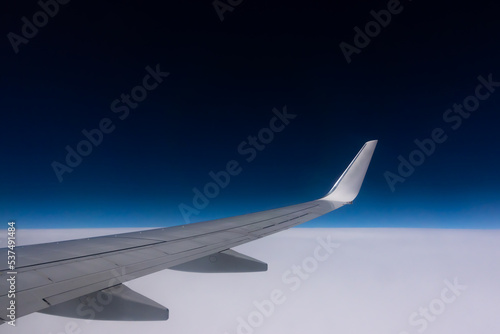 View from the plane window to the wing. Photo taken while flying above the clouds. In the distance, a visible horizon made of clouds