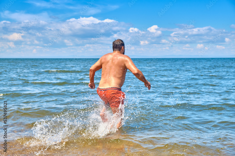 Fototapeta premium A young man runs into Lake Baikal. Siberia, Russia.