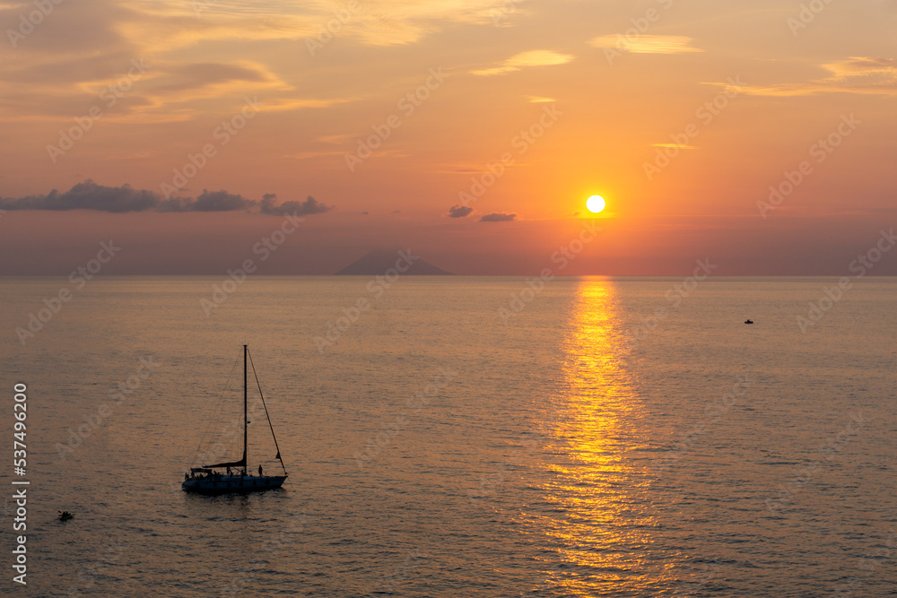 Tramonto sul mare, con vulcano Stromboli in lontananza e barca in mare, Tropea, Calabria, Italia