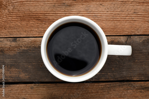White cup with coffee on a wooden table.
