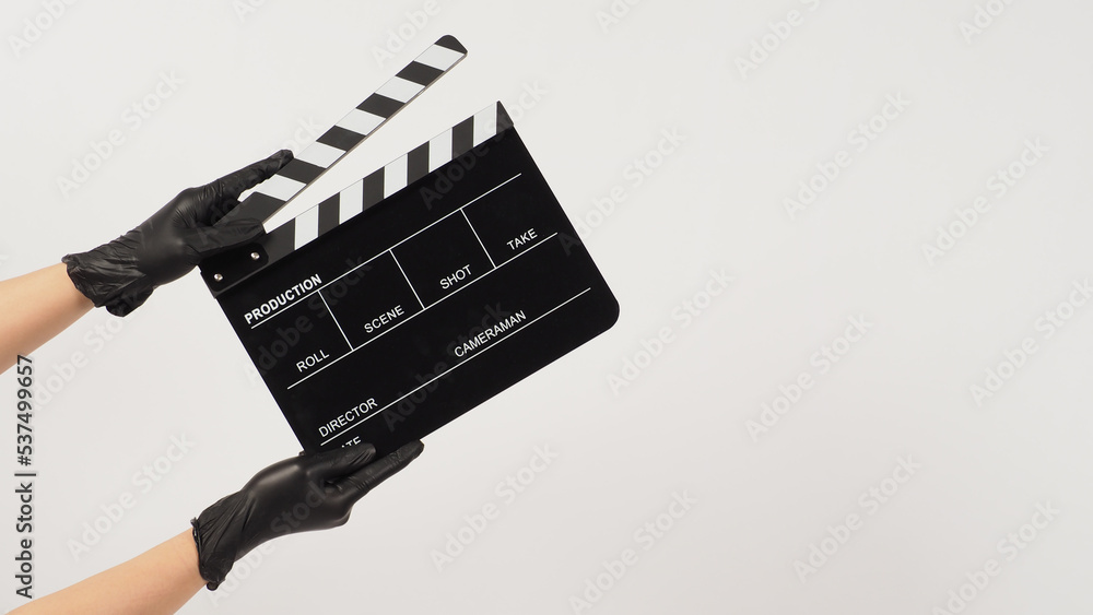 Naklejka premium Hand hold black clapper board or movie slate and wear black latex glove on white background.