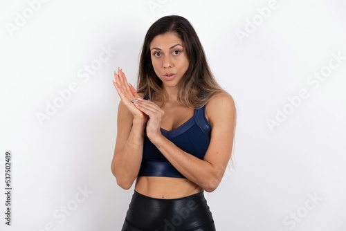 Surprised emotional young beautiful woman wearing sportswear over white background rubs palms and stares at camera with disbelief