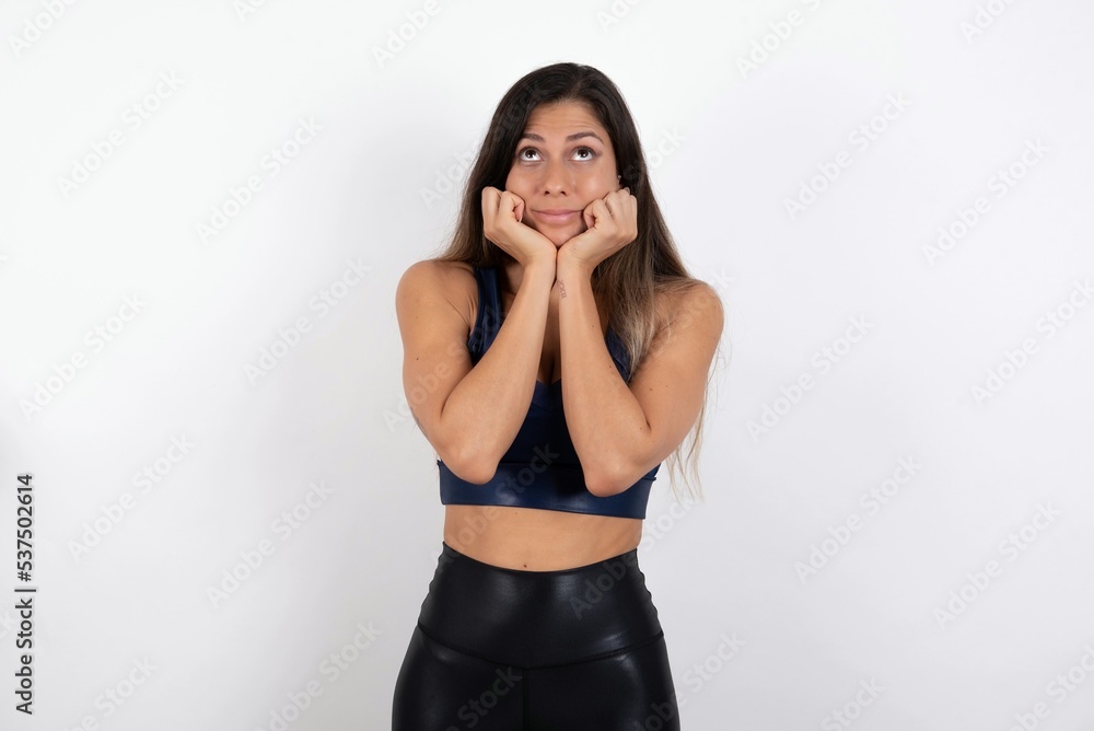 Portrait of sad young beautiful woman wearing sportswear over white background hands face look empty space Portrait of sad young beautiful woman wearing sportswear over white background hands face look empty space