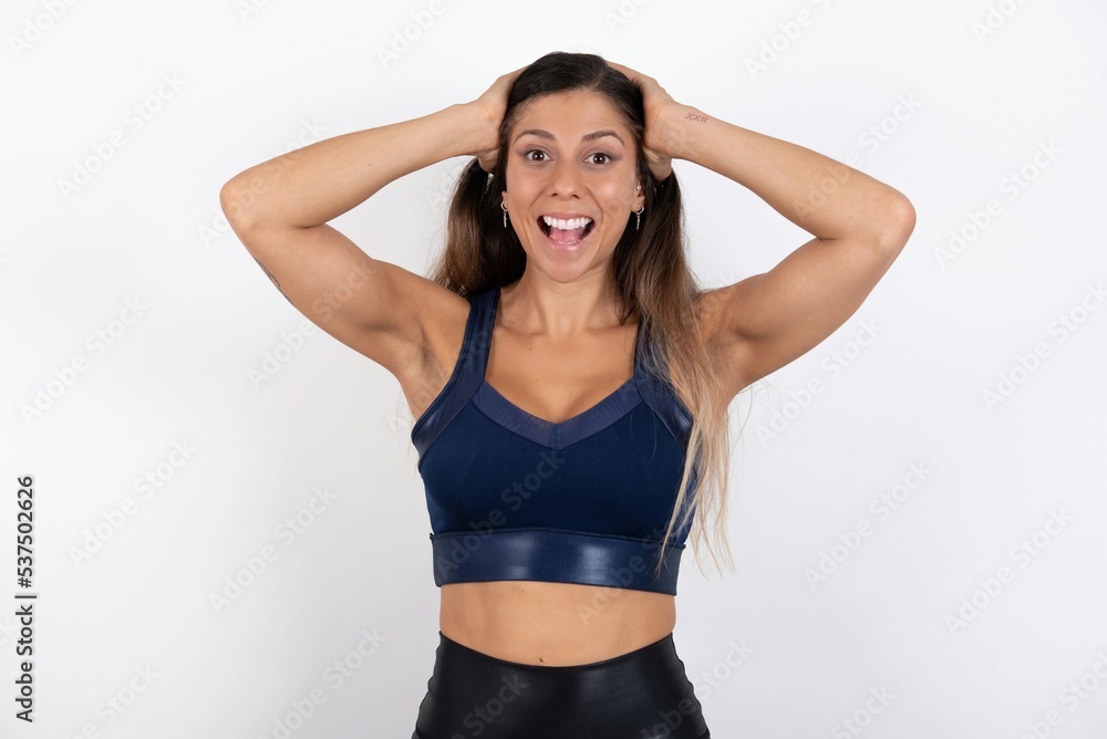 Cheerful overjoyed young beautiful woman wearing sportswear over white background reacts rising hands over head after receiving great news. Cheerful overjoyed young beautiful woman wearing sportswear over white background reacts rising hands over head after receiving great news.