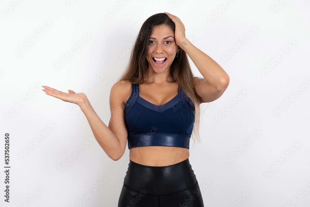 Shocked amazed surprised young beautiful woman wearing sportswear over white background hold hand offering proposition Shocked amazed surprised young beautiful woman wearing sportswear over white background hold hand offering proposition
