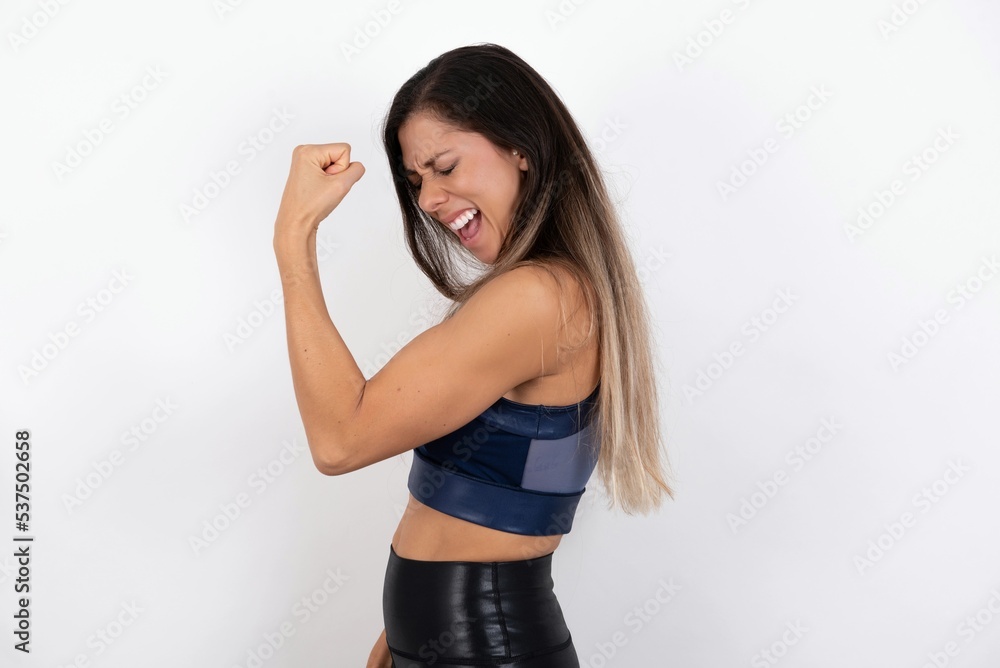Portrait of funny young beautiful woman wearing sportswear over white background shout yeah raise fists hands celebrate victory game competition Portrait of funny young beautiful woman wearing sportswear over white background shout yeah raise fists hands celebrate victory game competition