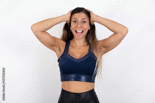 Cheerful overjoyed young beautiful woman wearing sportswear over white background reacts rising hands over head after receiving great news.