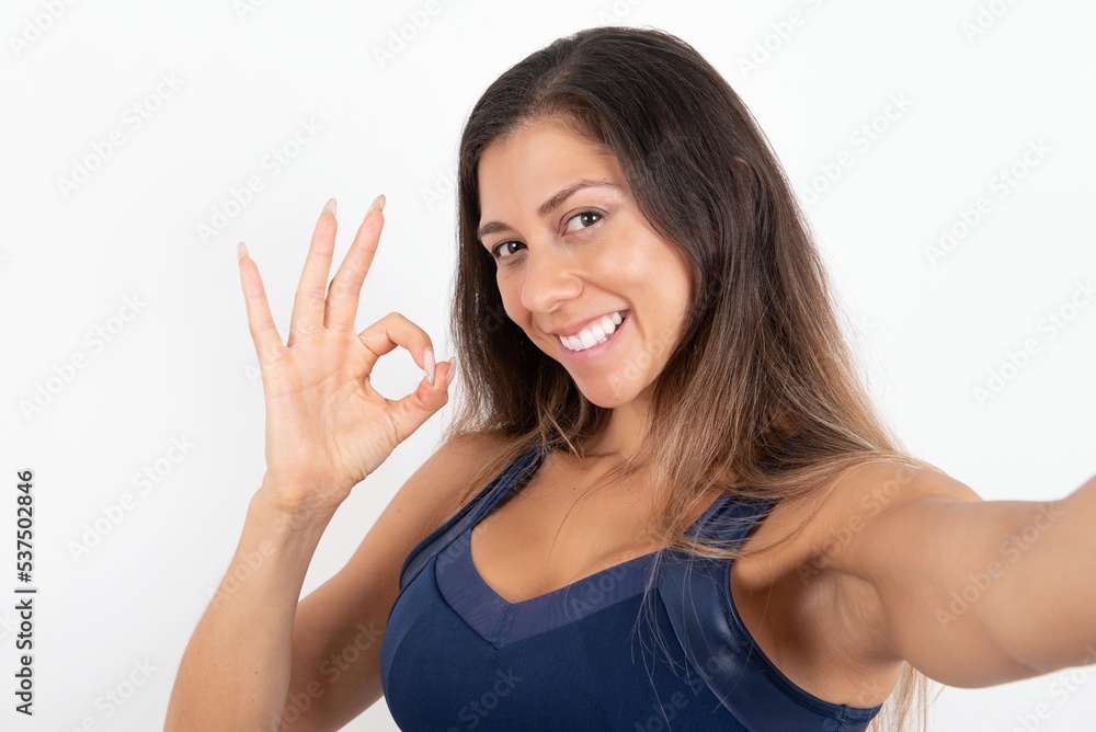 Portrait of pretty cheerful young beautiful woman wearing sportswear over white background make selfie show okey symbol Portrait of pretty cheerful young beautiful woman wearing sportswear over white background make selfie show okey symbol