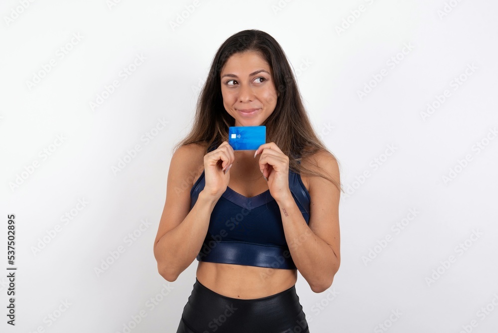 Photo of cheerful young beautiful woman wearing sportswear over white background hold debit card look empty space Photo of cheerful young beautiful woman wearing sportswear over white background hold debit card look empty space