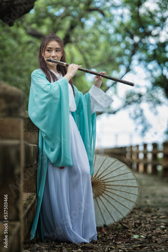 Portrait woman in a Chinese costume with a sword in the forest. Chinese girl with a traditional suit with a sharp sword in her hands. Beautiful and belligerent face.