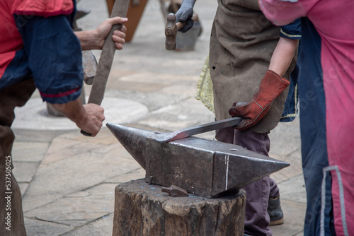 Plano detalle de dos hombres con guantes y delantal elaborando armas de manera artesanal sobre un yunque de hierro en el mercado medieval y de artesanía de Hondarribia en el País Vasco.