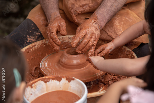 Plano detalle de las manos de un adulto y niños manchadas de barro trabajando y elaborando de manera tradicional objetos de barro cocido en el mercado medieval de Hondarribia en el País Vasco. photo