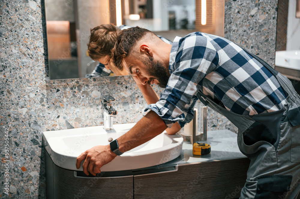 Feeling frustated. Works with sink. Plumber in uniform is indoors at home Feeling frustated. Works with sink. Plumber in uniform is indoors at home