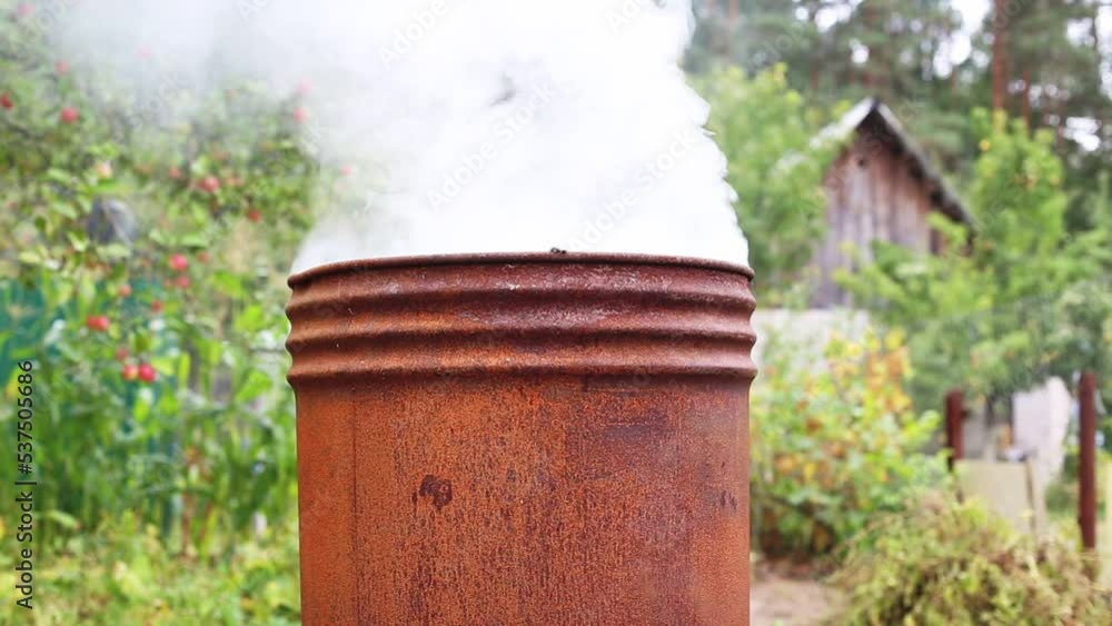 Burning weeds and grass in a barrel at the dacha against the backdrop of a garden and nature. A lot of smoke. The end of the summer season in autumn, agriculture. Copy space for text Burning weeds and grass in a barrel at the dacha against the backdrop of a garden and nature. A lot of smoke. The end of the summer season in autumn, agriculture. Copy space for text