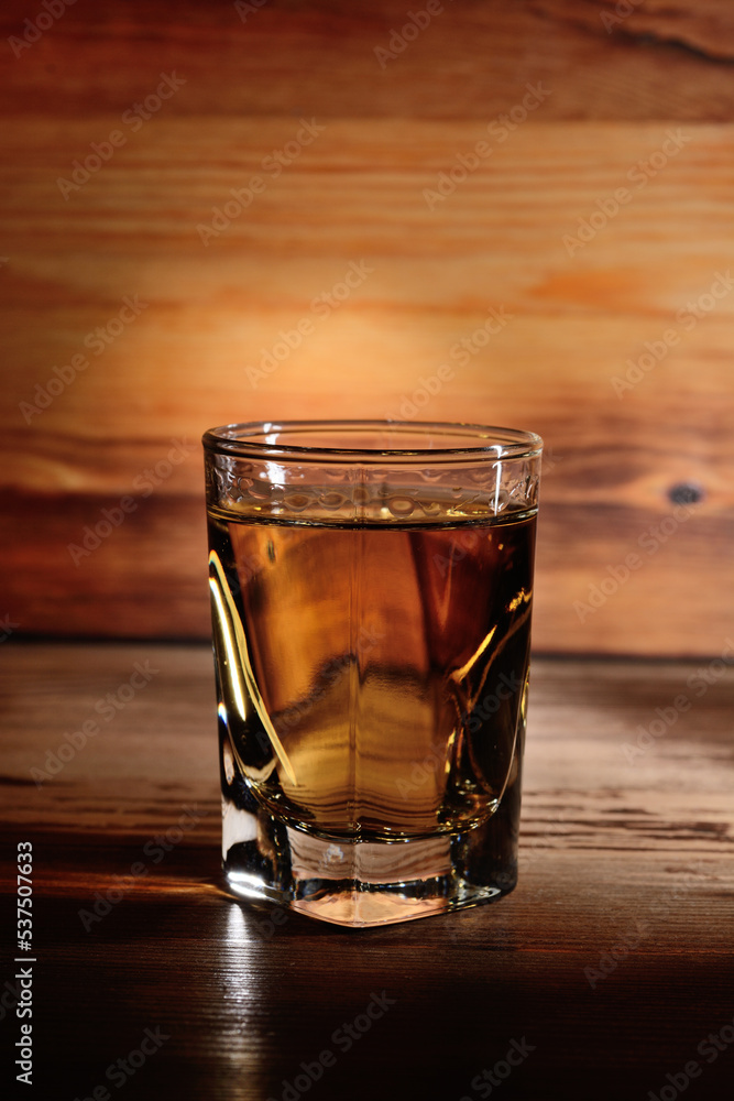A portion of aged alcohol in a glass, close-up against the background of a wooden structure. A portion of aged alcohol in a glass, close-up against the background of a wooden structure.