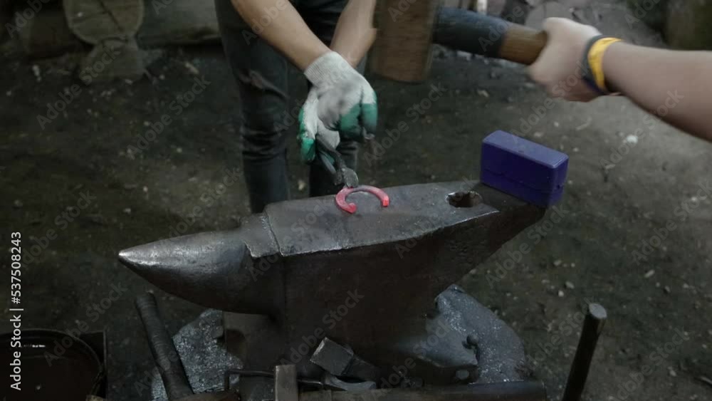 A blacksmith works in a forge on an anvil with a hammer, making a horseshoe for good luck, close-up A blacksmith works in a forge on an anvil with a hammer, making a horseshoe for good luck, close-up