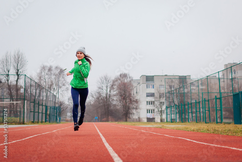 Young woman athlete running on sportsground in autumn. Full body portrait. Active healthy lifestyle